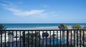 A beach view from a balcony with a pool and lounge chairs.