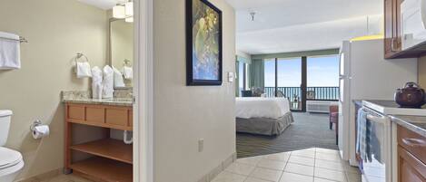 A hotel room with a bathroom, kitchenette, and a balcony with a view.