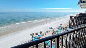 A beach view from a balcony with a railing, a sandy beach, and a clear blue sky.