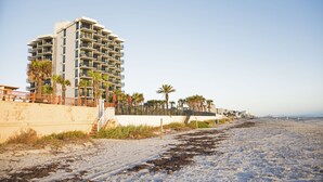 A beachfront hotel with multiple balconies, a sandy beach, and palm trees.