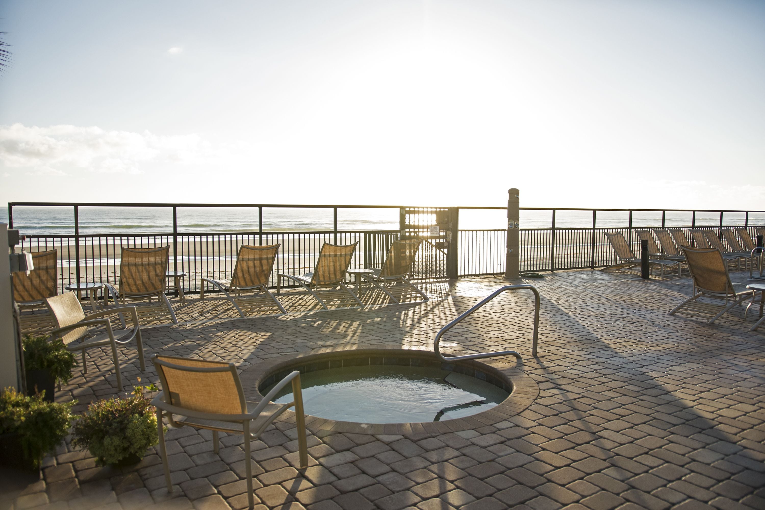 A sunlit outdoor seating area with a pool, chairs, and a view of the ocean.