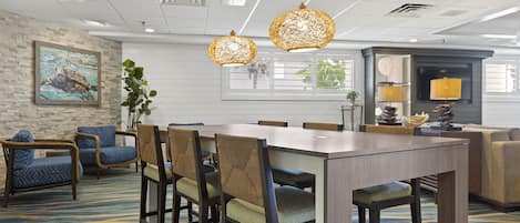 A hotel dining area with a long wooden table, six chairs, and two hanging light fixtures.