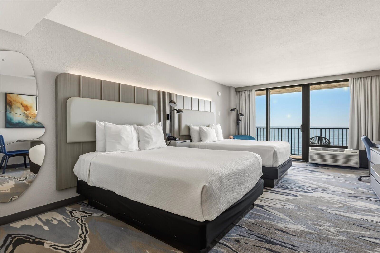 Quarto de hotel com duas camas, uma janela ampla com vista, uma escrivaninha e uma cadeira.