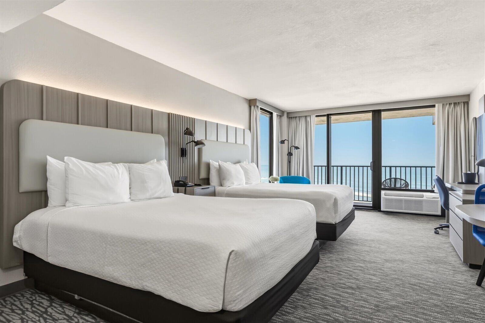 Une chambre d’hôtel avec deux lits, un bureau, une chaise, un balcon avec vue et une grande fenêtre.