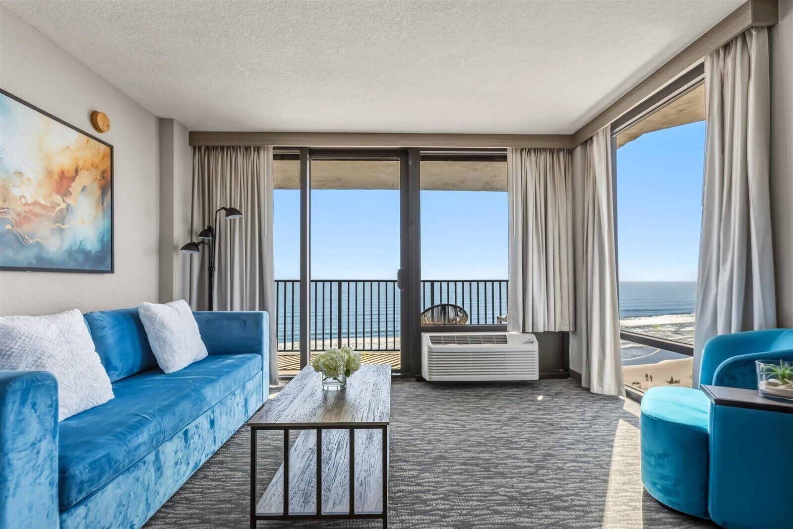 A balcony with a view of the beach, a blue sofa, a coffee table, and a chair.
