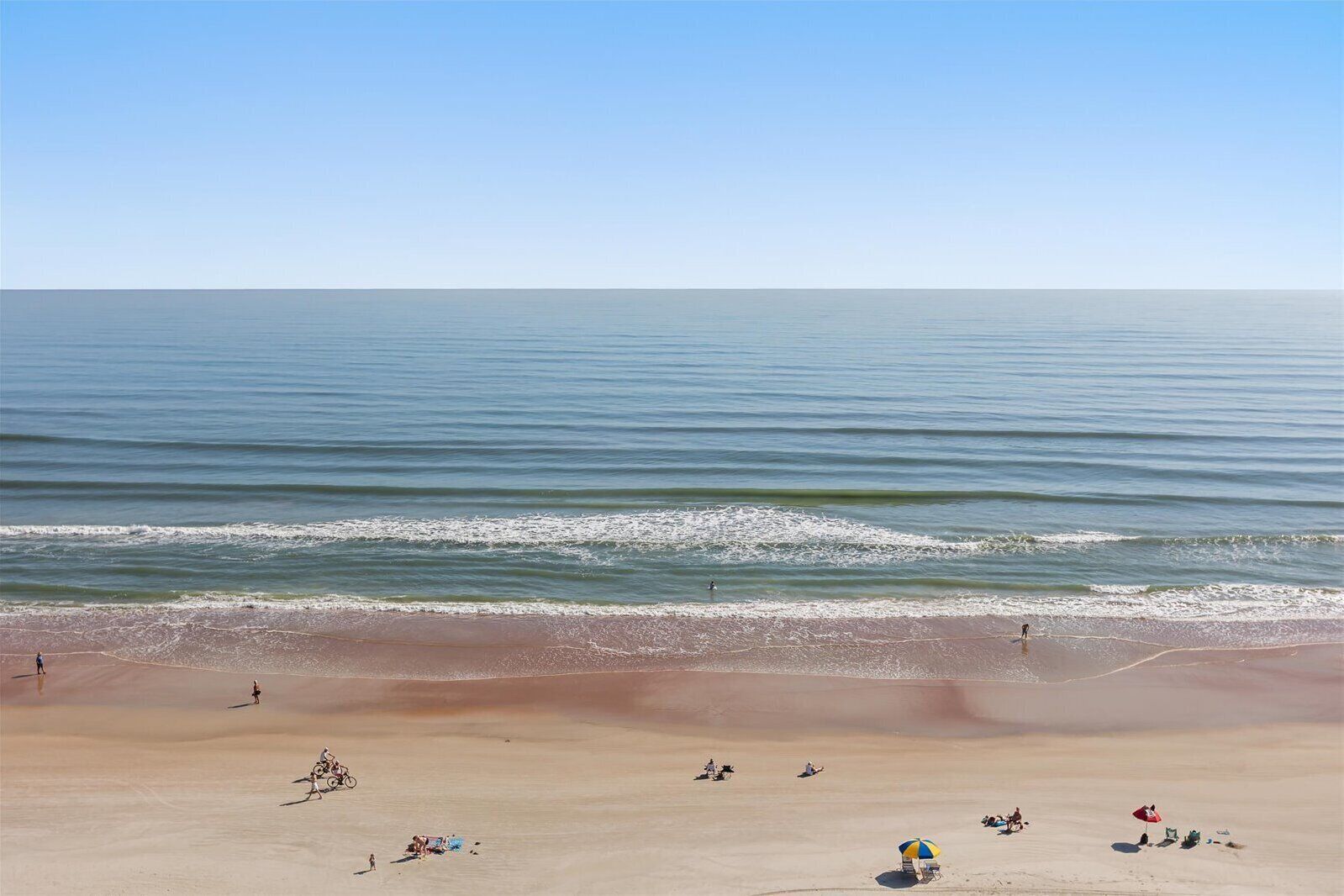 A beach with people, a bicycle, and a few umbrellas.