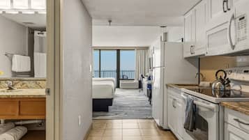 Quarto de hotel com banheiro, cozinha compacta e varanda com vista.