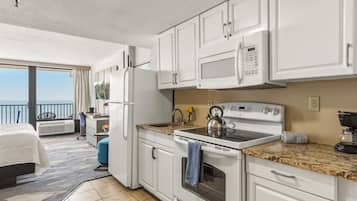 A modern kitchen with white cabinets, a microwave, stove, and a kettle. There's a balcony with a view.