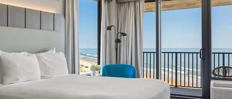 Una habitación de hotel con una cama grande, una silla azul, una mesita de noche, una lámpara y vistas a la playa.