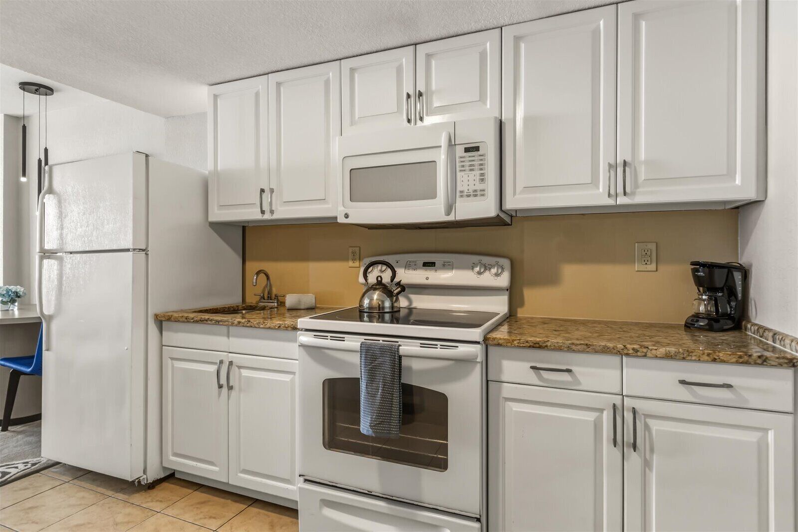 A kitchen with white cabinets, a microwave, a stove, and a coffee maker.