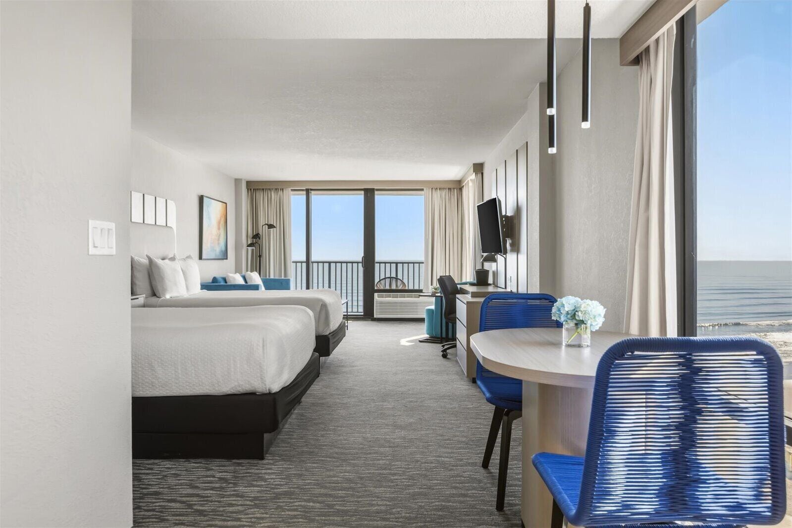 A hotel room with a bed, a desk, a chair, and a view of the ocean.