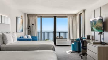 A hotel room with two beds, a desk, a chair, a TV, and a balcony with a view of the sea.