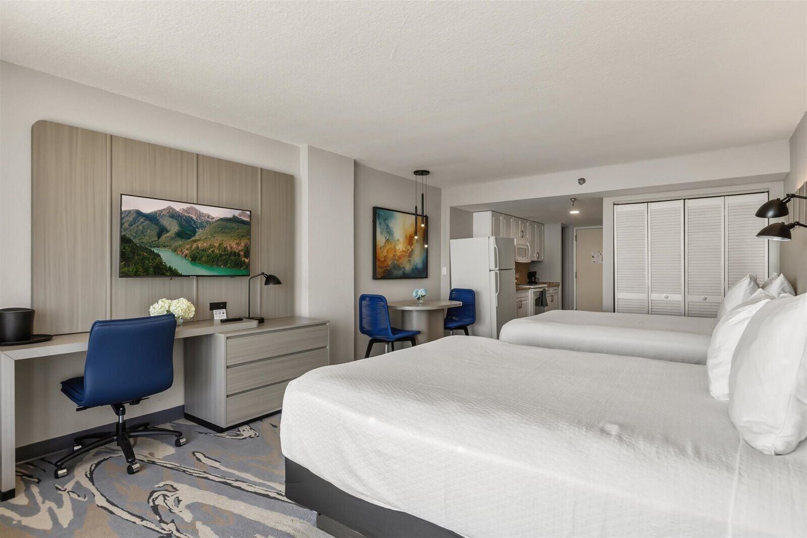 A hotel room with a bed, desk, chair, and a small kitchenette.