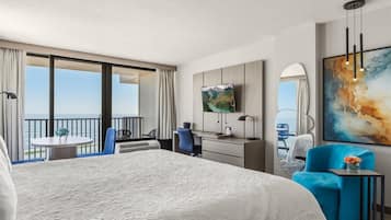 A hotel room with a large bed, a desk with a TV, a balcony with a table and chairs, and a painting on the wall.