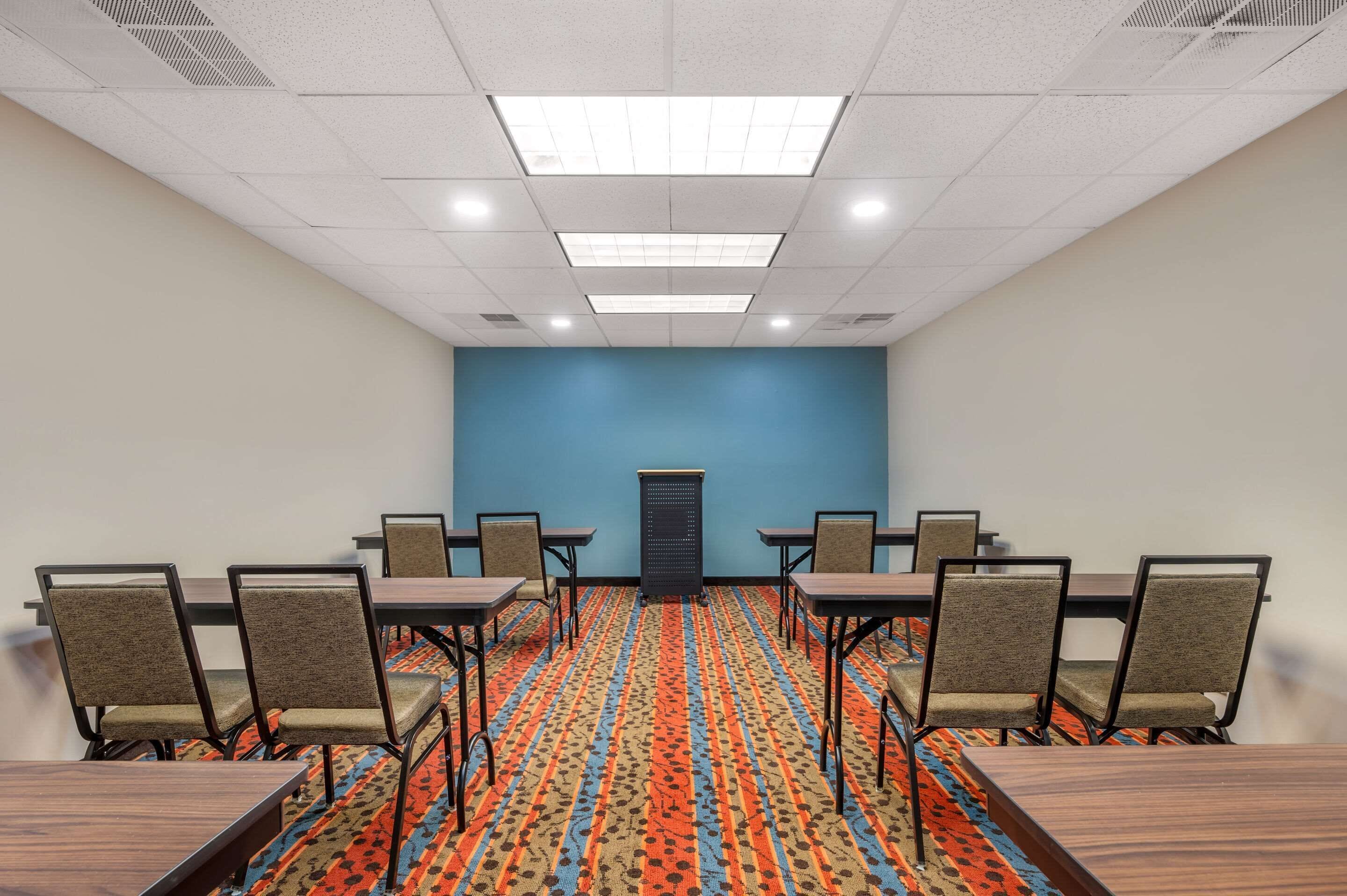 A conference room with a blue accent wall, patterned carpet, and a row of chairs and tables.
