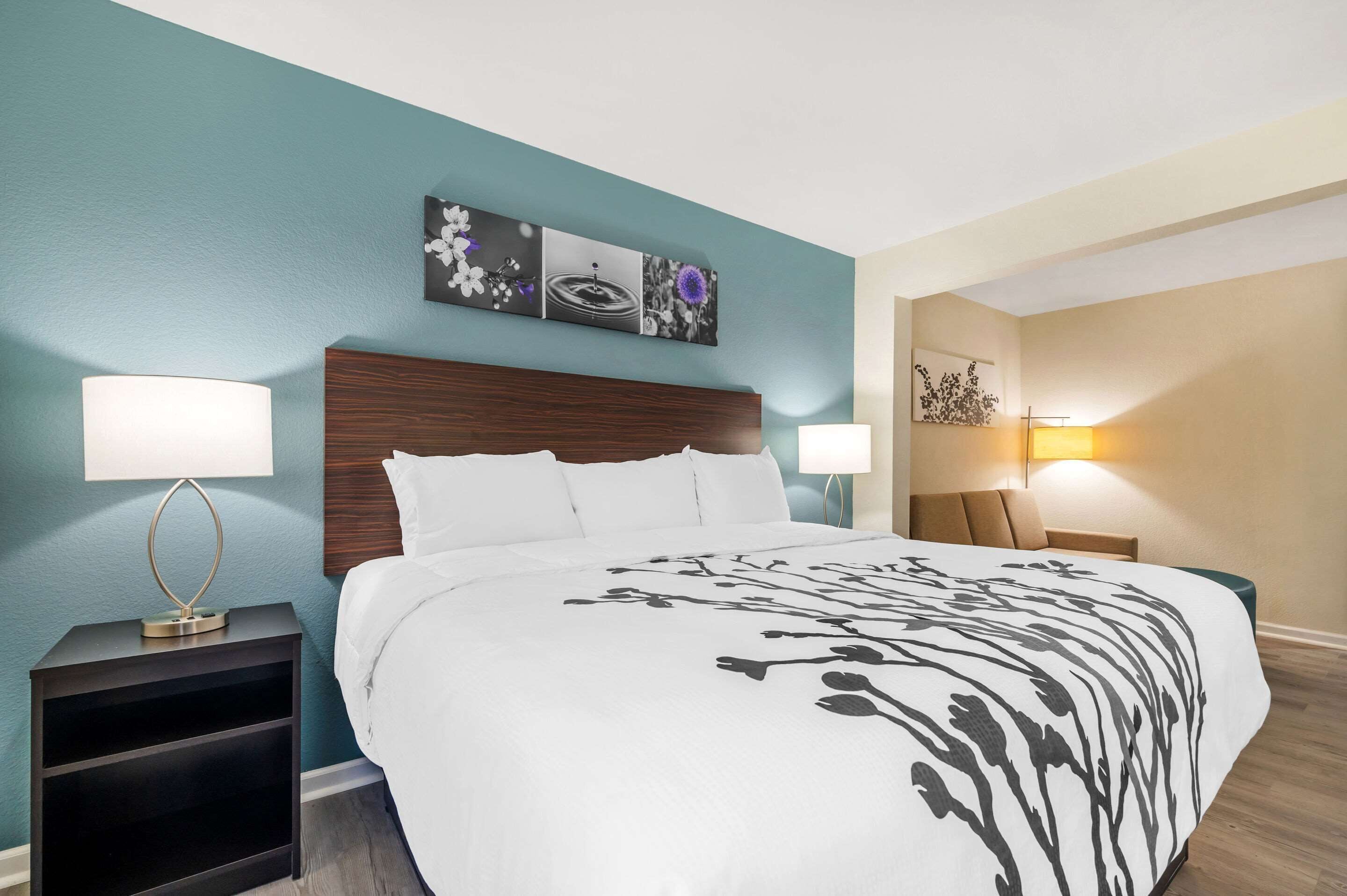 A hotel room with a bed, two bedside tables, a nightstand, and a wall-mounted artwork above the bed.