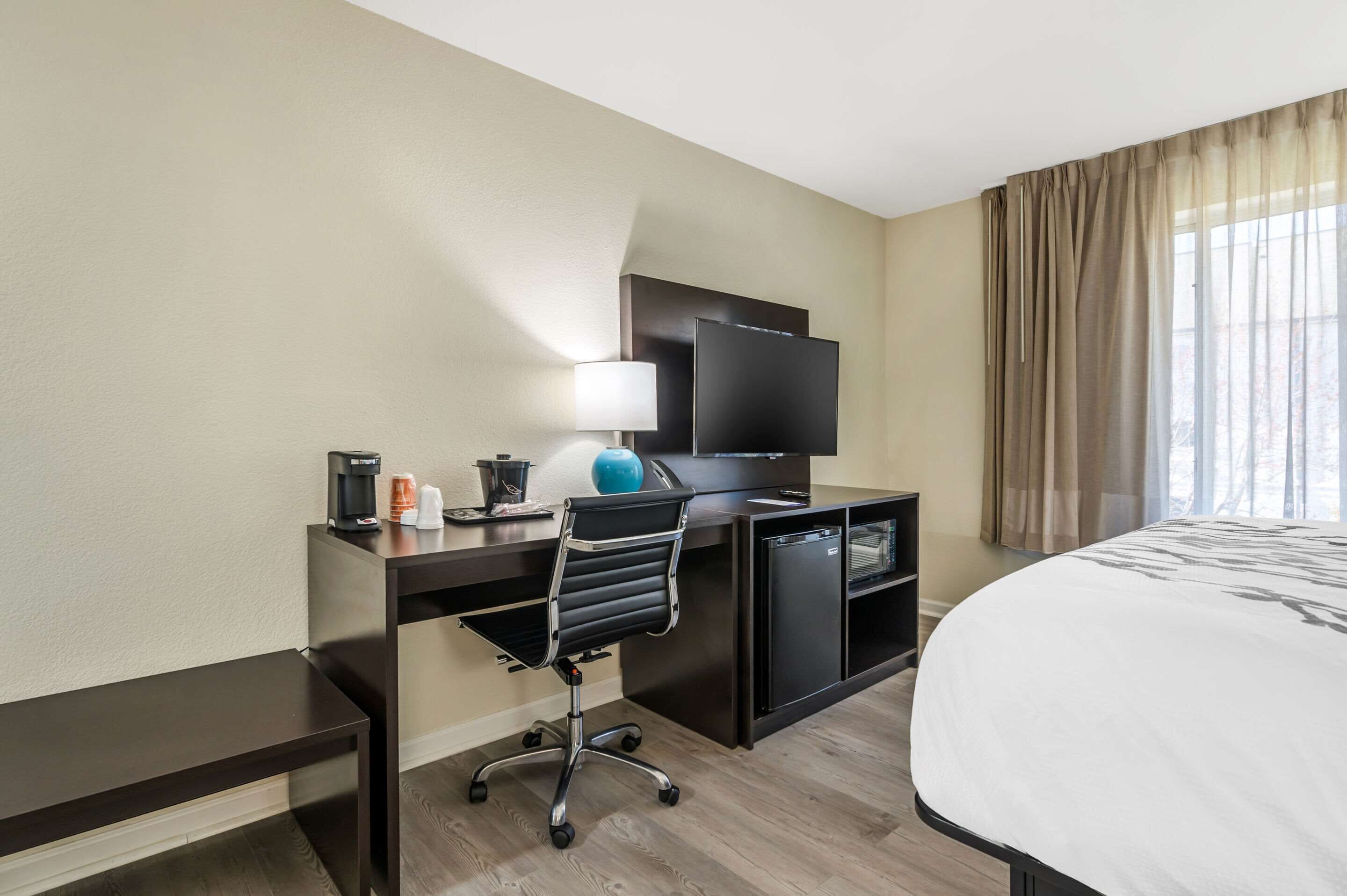 A hotel room with a bed, a desk with a computer, a television, a lamp, and a coffee maker.