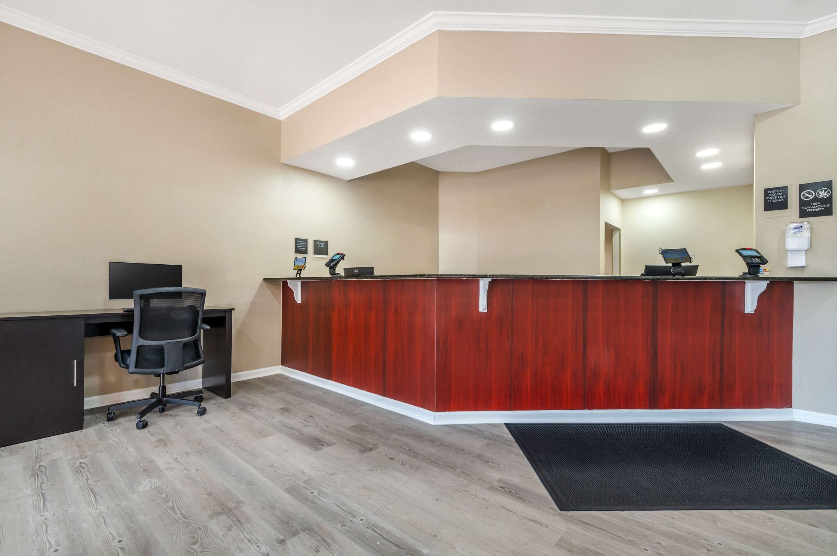 A reception area with a wooden reception desk, a black office chair, a desk with a computer, and a black mat on the floor.