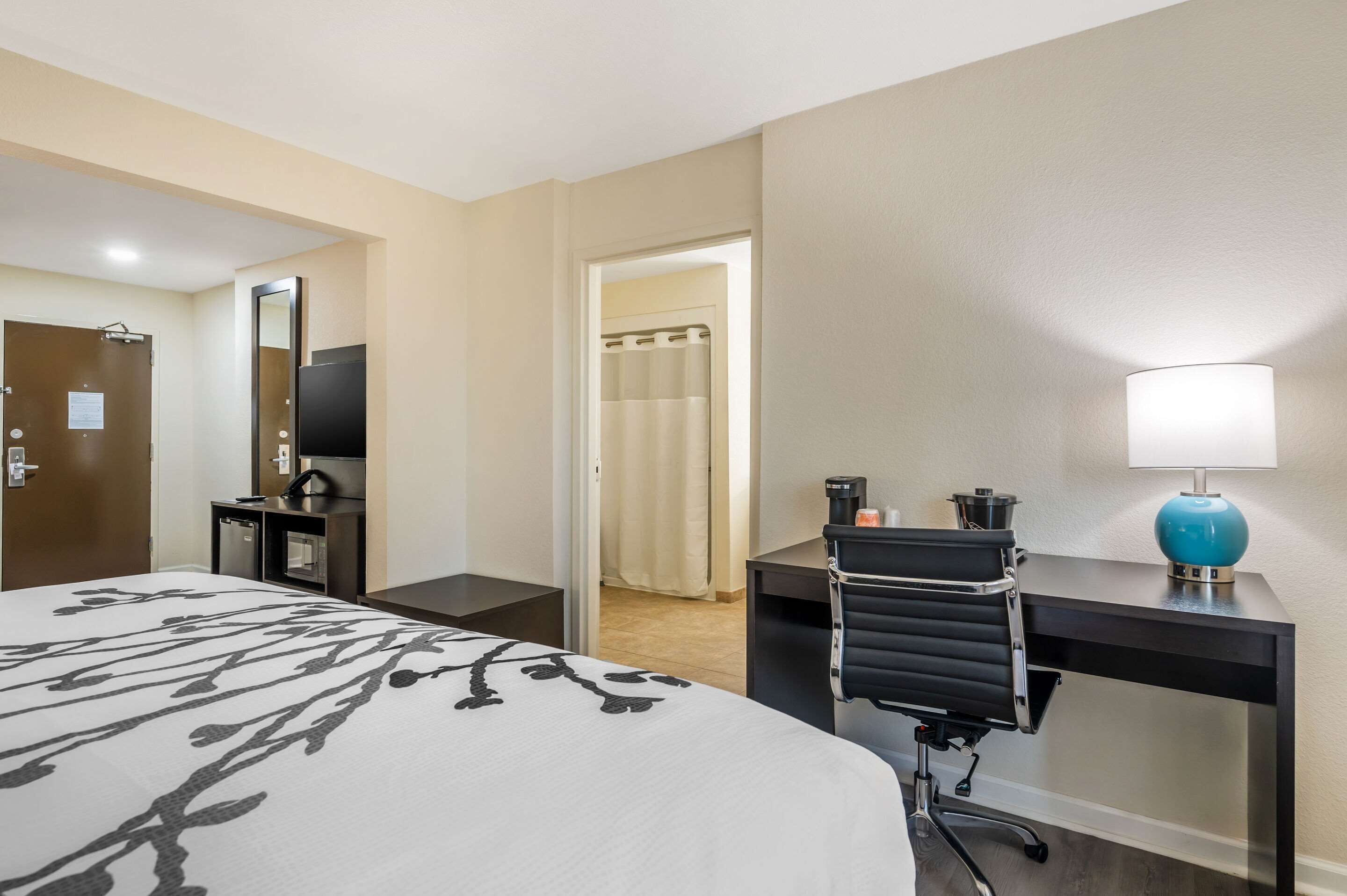 A hotel room with a bed, desk, chair, lamp, and a bathroom visible through an open door.