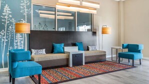Eine moderne Hotelhalle mit einer Sofagarnitur, zwei Sesseln, einem kleinen Tisch und einem gemusterten Teppich.