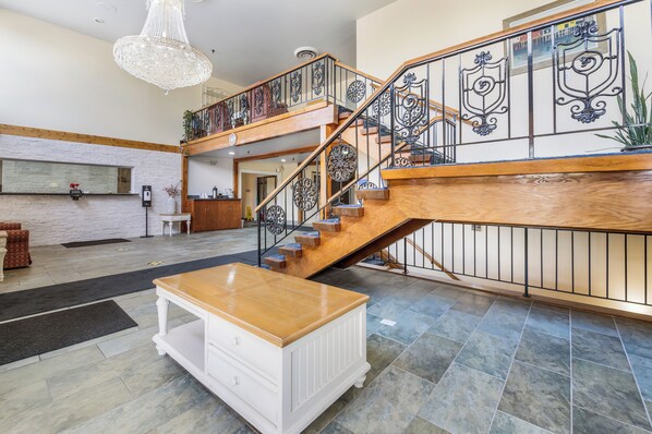 A spacious lobby with a wooden staircase, a chandelier, and a reception desk. - Equality Inn (Rockford)