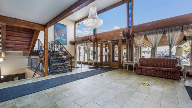 A spacious lobby with a staircase, a chandelier, and a large window offering a view of the outside.
