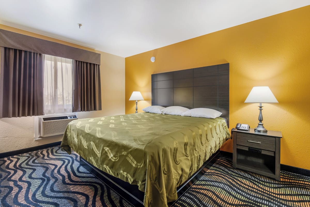 A hotel room with a bed, two bedside lamps, a nightstand, and a window with curtains.