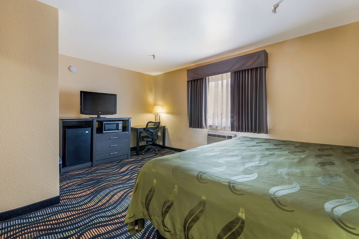 A hotel room with a bed, a desk with a television, a microwave, and a small refrigerator.
