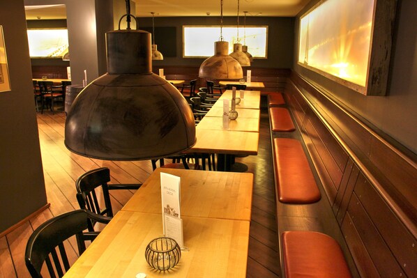A restaurant interior with wooden tables, benches, and hanging pendant lights. - Hotel Park Soltau (Soltau)