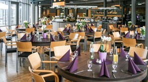 A modern restaurant with round tables, wooden chairs, and purple napkins. - Hotel Park Soltau (Soltau)