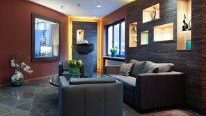 A modern living room with a sofa, a coffee table, and a decorative bowl. There are shelves with decorative items and a large mirror on the wall. - Hotel Park Soltau (Soltau)