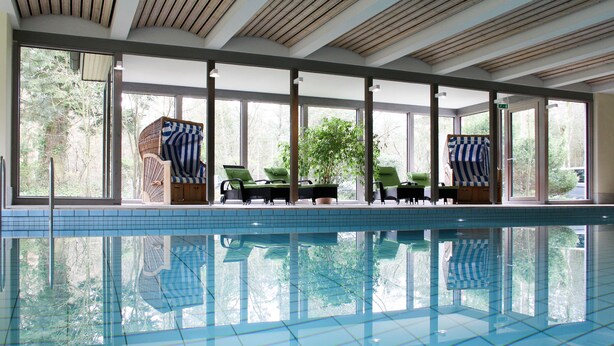 A large indoor swimming pool with clear blue water, surrounded by large windows and lounge chairs. - Hotel Park Soltau (Soltau)