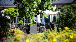 An outdoor seating area with tables and chairs, surrounded by lush greenery and flowering plants. - Hotel Park Soltau (Soltau)