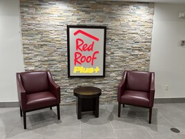 Señal Red Roof Plus sobre una pared de piedra, dos sillones de cuero y una pequeña mesa redonda en un área de recepción.