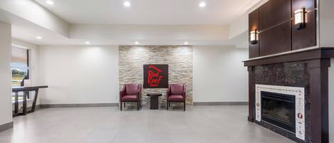 Um hall amplo com parede de pedra, duas poltronas de couro, uma pequena mesa e uma lareira.