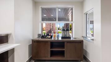 Een keurige, moderne kitchenette met een ingebouwde koffiemachine, een koffieautomaat en een kleine keuze aan toevoegingen.