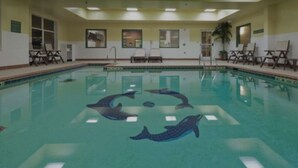 Une piscine intérieure décorée de motifs de dauphins en mosaïque, dotée de chaises longues et d’un plafond équipé d’un système d’éclairage encastré.