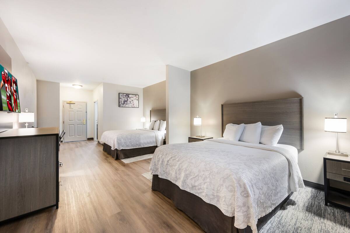 Una habitación de hotel con una cama grande, una cama más pequeña, un escritorio y una silla. Hay una puerta que da a otra habitación.