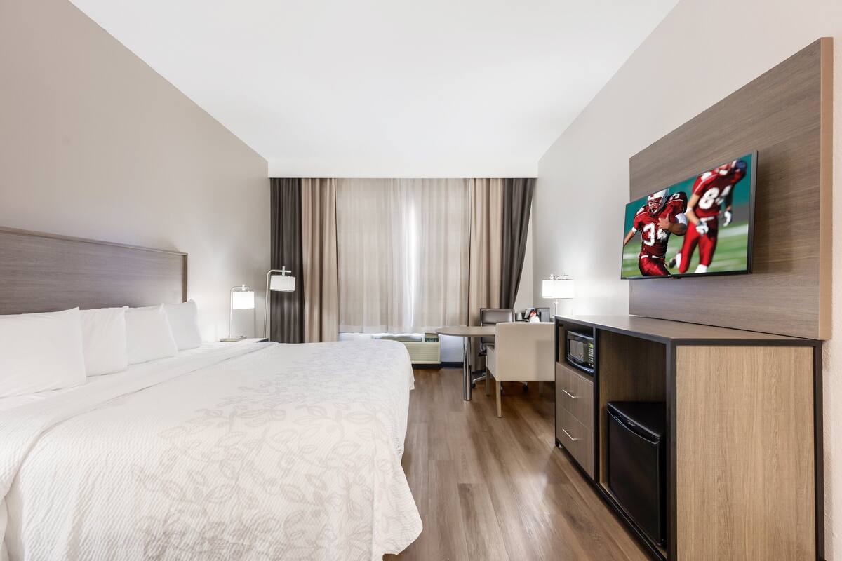 Una habitación de hotel con una cama grande, un escritorio, un televisor y un refrigerador.