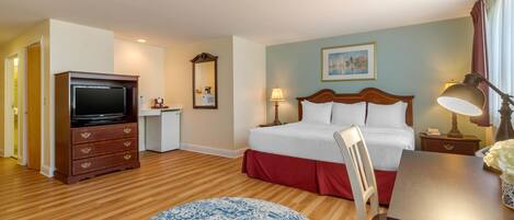 A hotel room with a bed, a desk, a television, a chair, and a round rug.