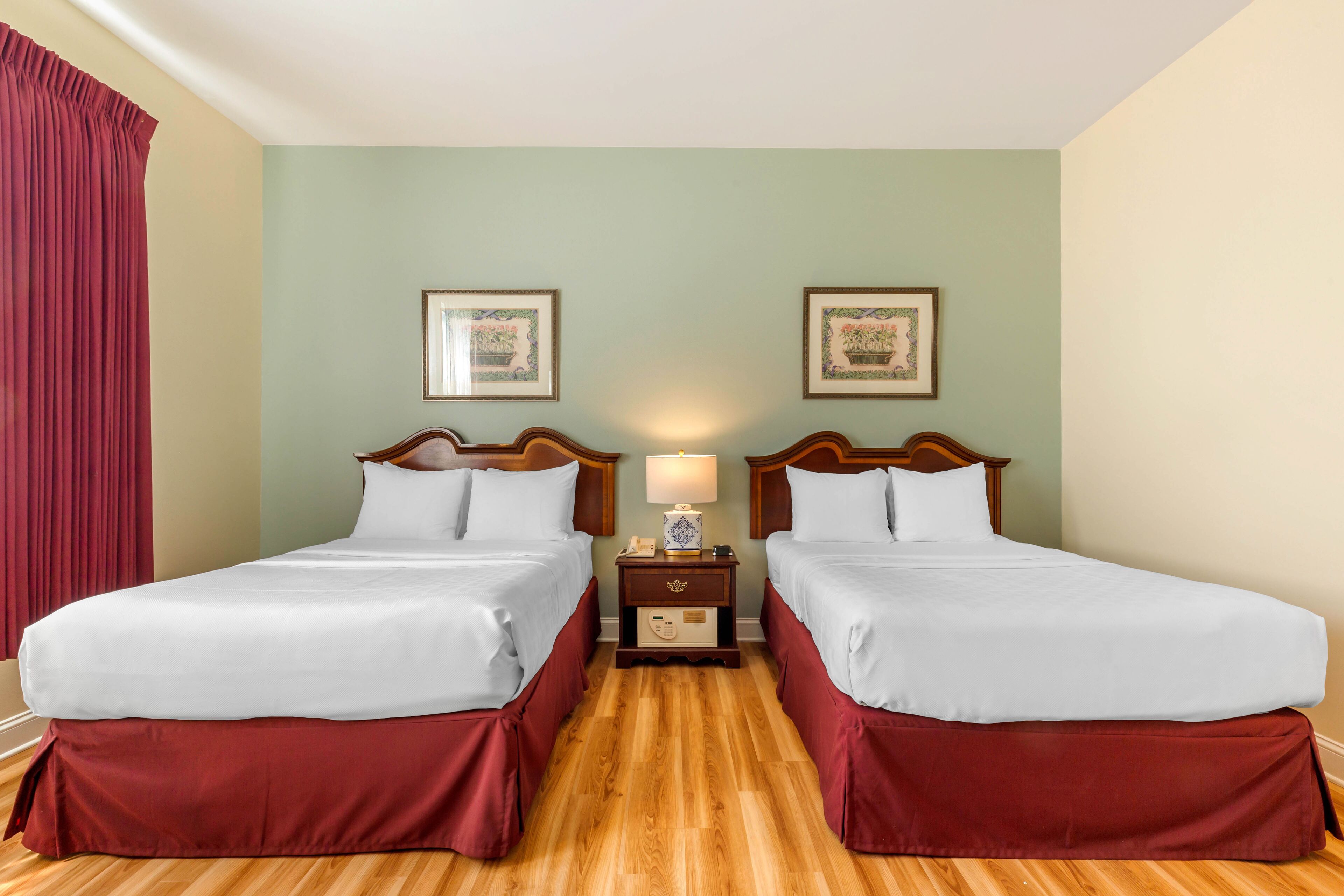 A hotel room with two beds, wooden headboards, a nightstand with a lamp, and two framed pictures on the wall.