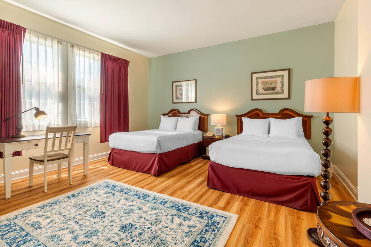 A hotel room with two beds, a desk, a chair, and a large blue patterned rug.
