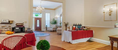 Un salón amplio con suelo de madera, una mesa de comedor con sillas, una mesa cubierta con mantel rojo y una araña.