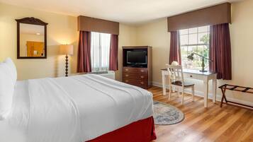 Une chambre d’hôtel avec un lit, un bureau, une chaise, une télévision et une fenêtre avec des rideaux.