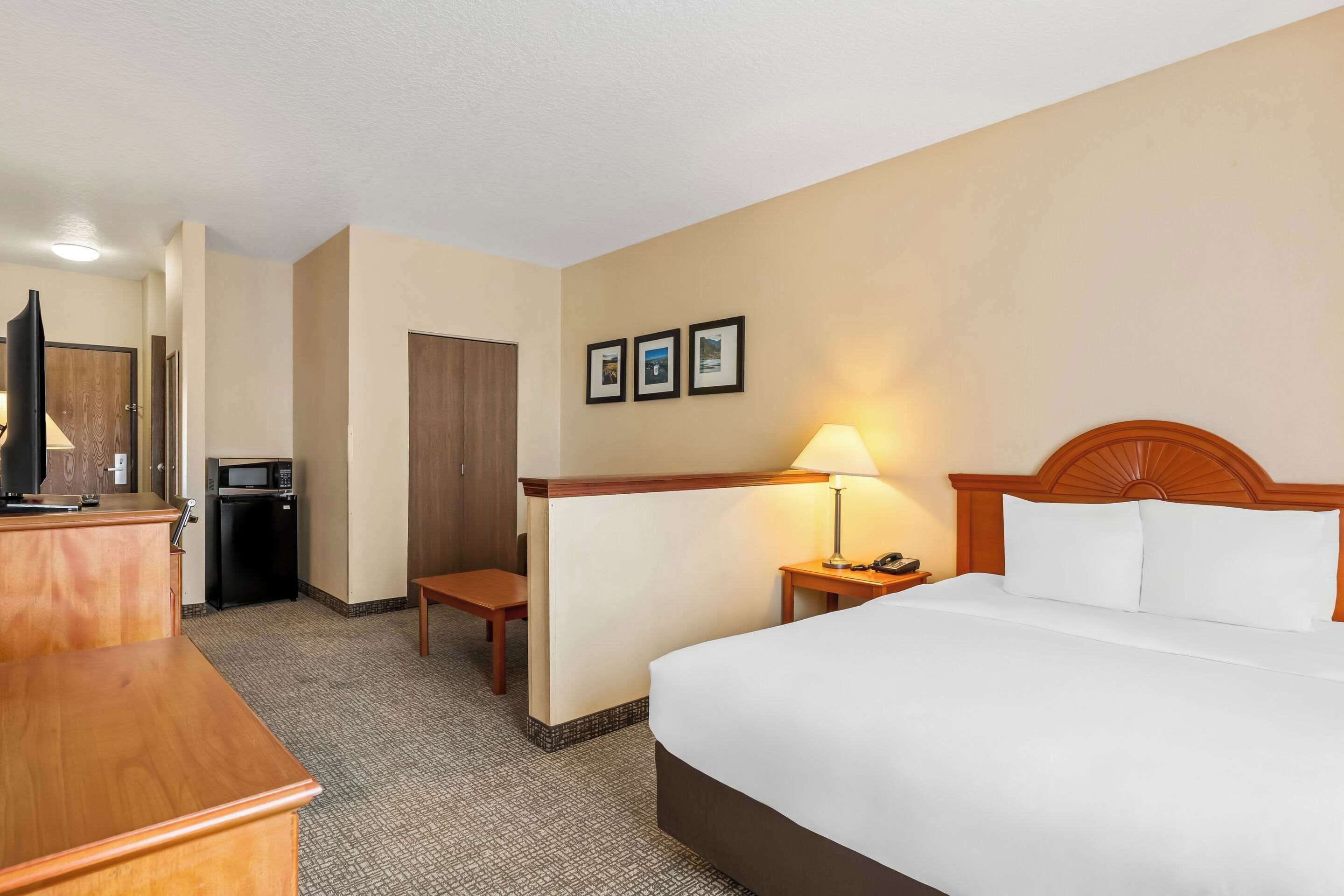 A hotel room with a bed, a desk, a chair, a microwave, and a lamp.
