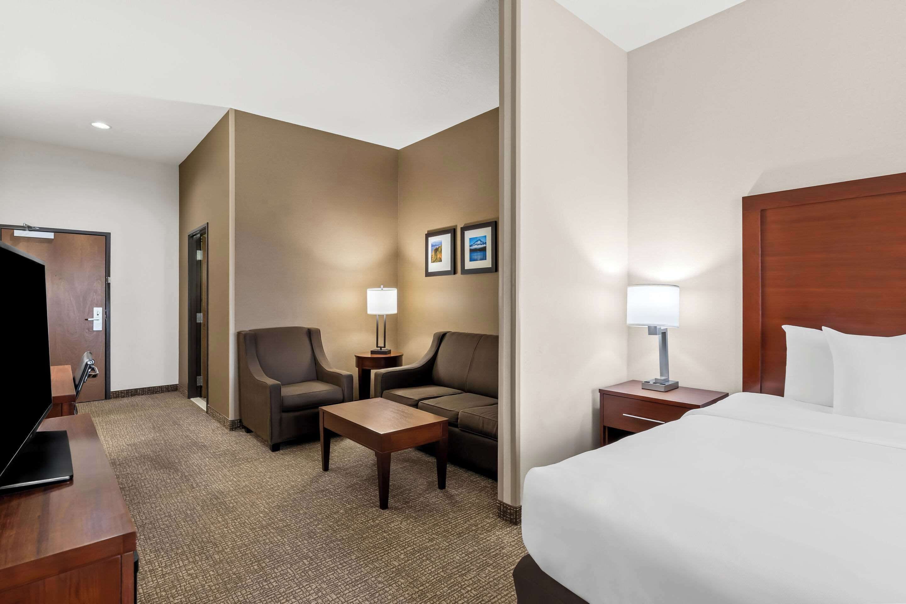 Une chambre d’hôtel comprenant un lit, deux fauteuils, une petite table, un téléviseur et une table de chevet avec une lampe.