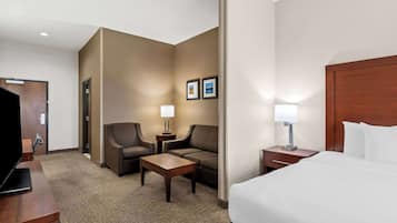 Une chambre d’hôtel comprenant un lit, deux fauteuils, une petite table, un téléviseur et une table de chevet avec une lampe.