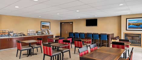 A hotel dining area with multiple tables and chairs, a coffee station, and a fireplace.