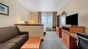 Een hotelkamer met een bank, een houten tafel, een televisie, een bureau met lades en een raam met gordijnen.