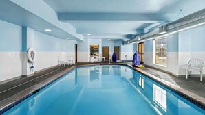 A swimming pool with clear blue water, white chairs, and a blue towel on the right side.